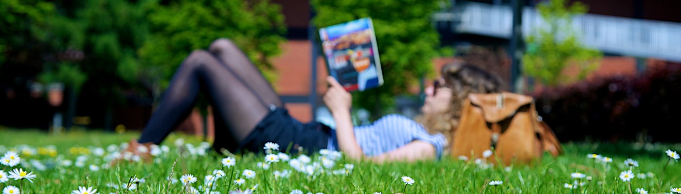 A female student lying on the grass reading a book 