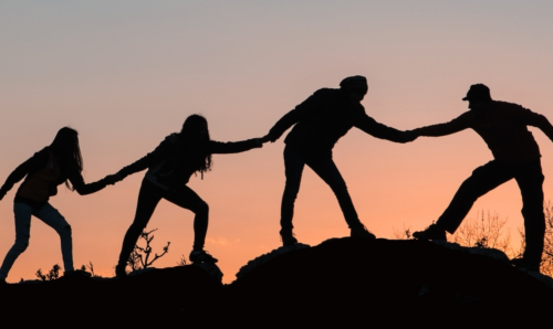 Four people holding hands on a hill at sunset