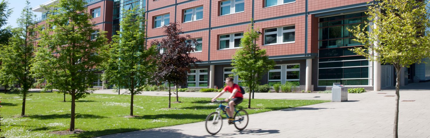 Student cycling past Arthur Lewis building 
