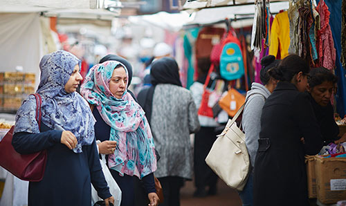 Two women looking at an outdoor market.