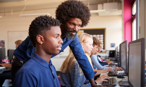 A student looking at a computer screen with a teacher helping.