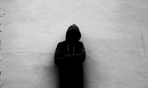 A hooded figure against a wall, image in black and white.
