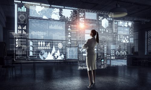 A woman stood looking at virtual screens showing charts and graphics.