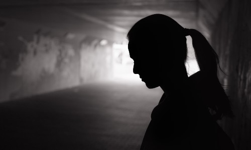 A person looking sad stood in a dark tunnel.