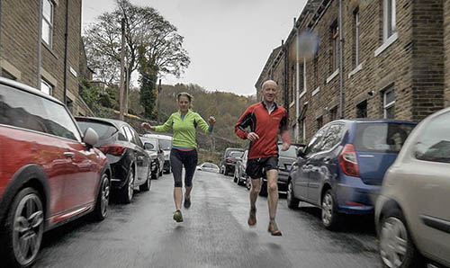 Middle aged couple jogging through a rainy residential street with cars parked on either side
