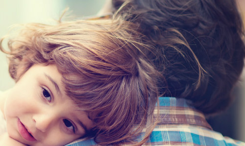 A young girl looking over her father's shoulder. 