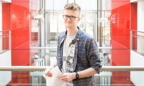 Male student smiling at the camera with a pen and paper